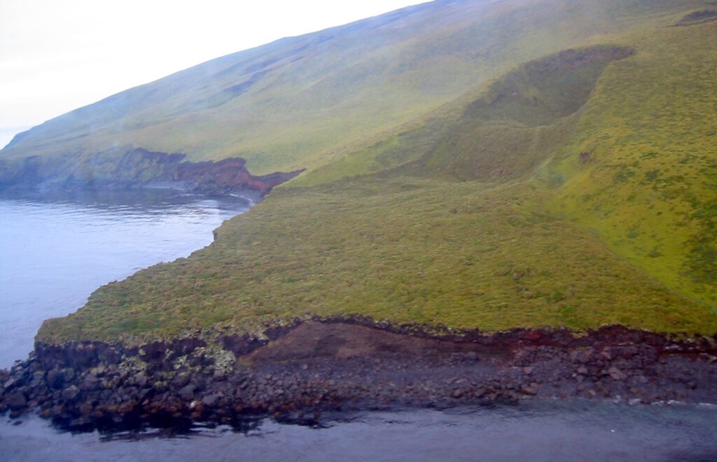 Un cratère et son delta de lave enherbé sur la côte d'une île volcanique.